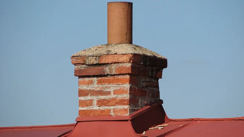 Brick chimney with a metal cap rising from a red metal roof