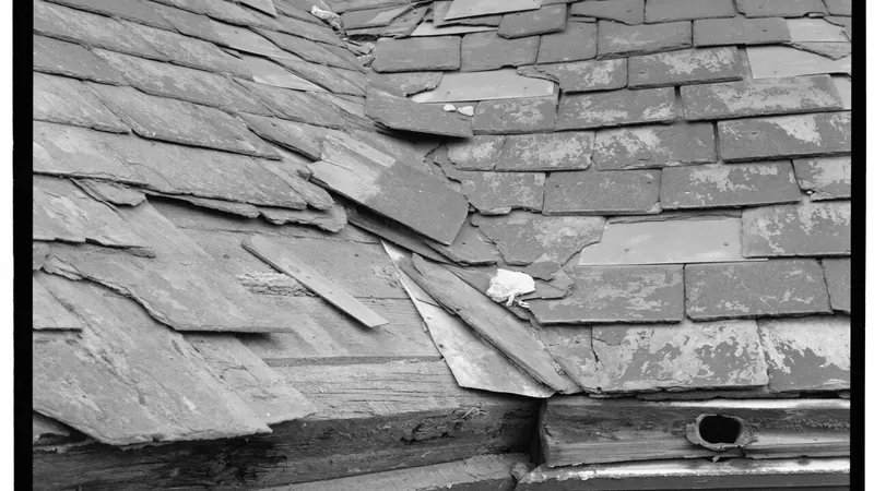 Black-and-white detail of a worn slate roof where two roof sections meet